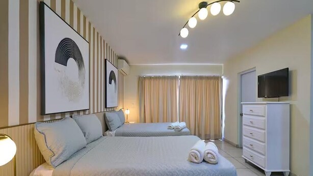Une chambre d’hôtel avec deux lits, une télévision, une commode et des œuvres d’art accrochées au mur.