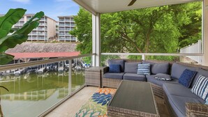 Ein überdachter Balkon mit einer Couch, einem Tisch und Blick auf einen Yachthafen und Gebäude.