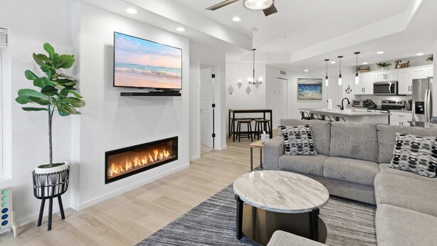 Ein modernes Wohnzimmer mit Kamin, Deckenventilator, Flachbildfernseher und Essbereich.