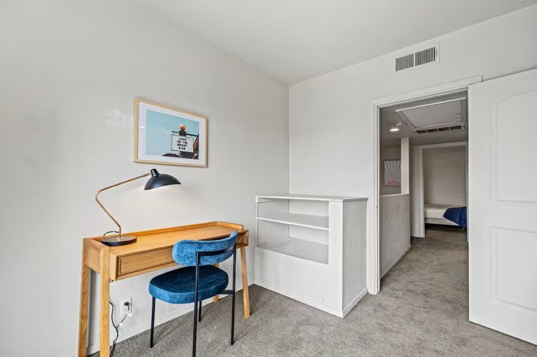 A bedroom with a bed, a desk with a chair, a wardrobe, and a door leading to another room.