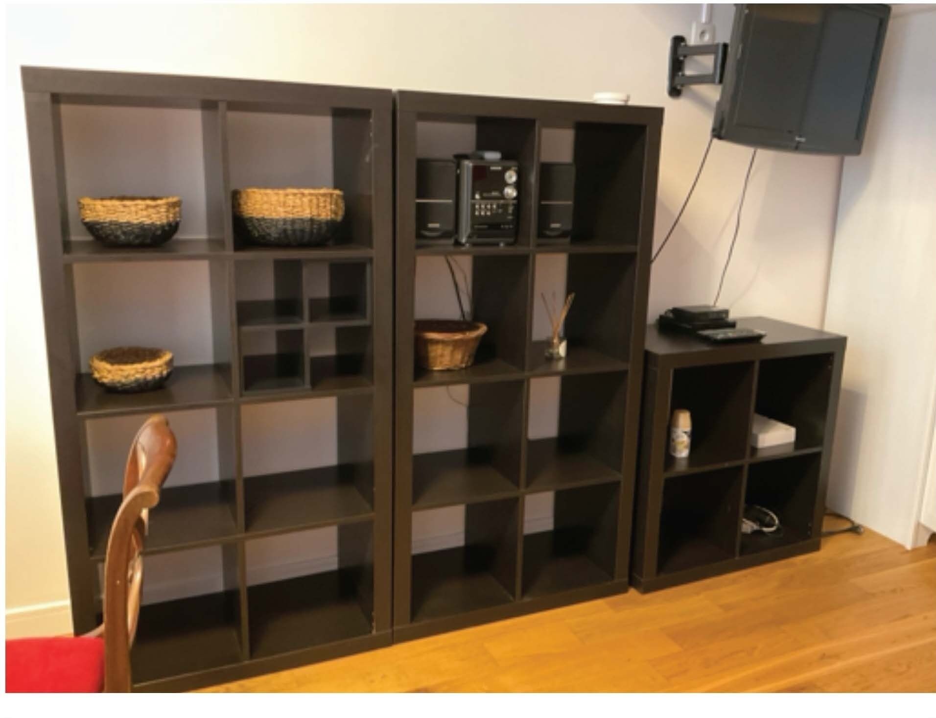 Ein Zimmer mit einer dunklen Holzeinrichtung, darunter Regale mit Körben, einem Radio und einem kleinen Tisch mit einer Fernbedienung.