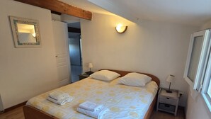 A bedroom with a wooden bed, a nightstand, a wall-mounted lamp, and a mirror. - CASA FOCI -  maison T3 (Sainte Lucie de Porto Vecchio)