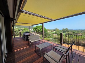 A wooden deck with a table and chairs, a covered area with a yellow canopy, and a view of a green landscape. - CASA FUNTA - villa T5 - vue mer- piscine (Sainte Lucie Porto-Vecchio)