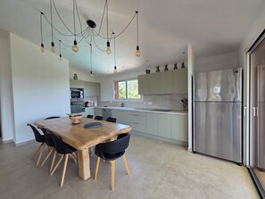 A modern kitchen with a dining area, stainless steel appliances, and pendant lighting. - CASA FUNTA - villa T5 - vue mer- piscine (Sainte Lucie Porto-Vecchio)