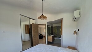 A bedroom with a bed, a wardrobe, a bathroom with a mirror, and a hanging light fixture. - CASA FUNTA - villa T5 - vue mer- piscine (Sainte Lucie Porto-Vecchio)