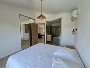 A bedroom with a bed, a wardrobe, a bathroom with a mirror, and a hanging light fixture. - CASA FUNTA - villa T5 - vue mer- piscine (Sainte Lucie Porto-Vecchio)