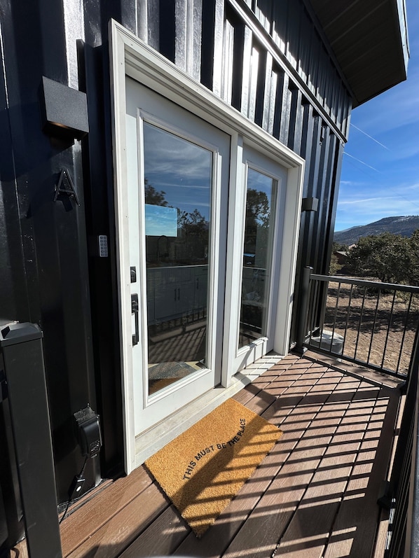 A modern building with a large sliding glass door, a doormat with a welcome message, and a metal railing on the balcony. - Container Home at the Edge of the San Juans (South Fork)