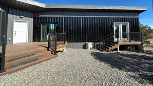 Een modern gebouw met een metalen gevel, een houten terras en een grindpad.
