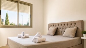 A neatly made bed with a headboard, a window with blinds, and a potted plant on a bedside table. - Luxury Oasis S 2 Comfort at the Garden in Carthage (Tunis)