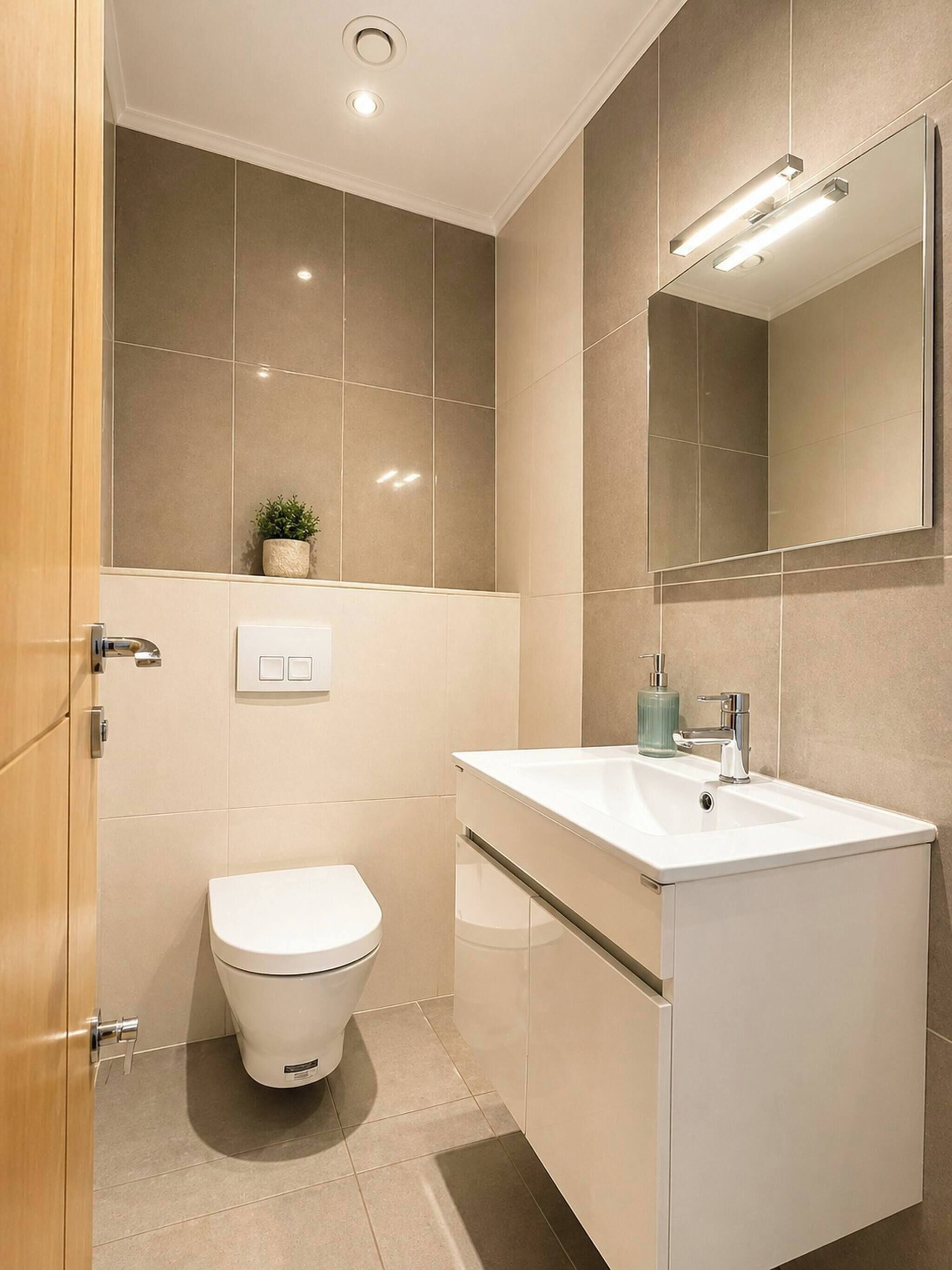 A modern bathroom with a toilet, sink, mirror, and recessed ceiling light.