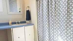 Un baño con inodoro, lavamanos con encimera azul, cortina de ducha estampada, espejo y toallero.
