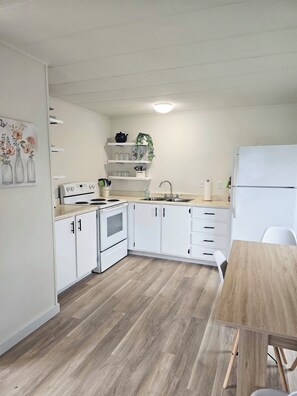 Una cocina con armarios blancos, una estufa, un lavamanos y una mesa de comedor de madera.