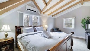 Une chambre à coucher avec un lit en bois, deux fenêtres, une table de chevet, une lampe et une plante.