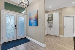 A modern interior with frosted glass doors, a blue mat at the entrance, a painting on the wall, and white cabinets. - Elegant 4-bed Home w/ Pool & Spa Near Anna Maria (West Bradenton)