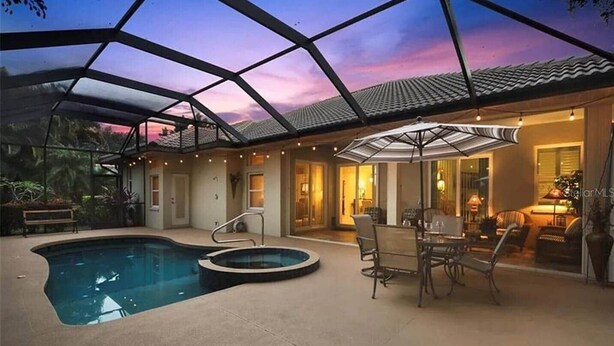 A covered outdoor pool area with a hot tub, seating, and a patio with a table and chairs. - Elegant 4-bed Home w/ Pool & Spa Near Siesta Key (Bee Ridge)