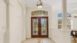 A hallway with a double door, a chandelier, and a dining area with a table and chairs. - Elegant 4-bed Home w/ Pool & Spa Near Siesta Key (Bee Ridge)