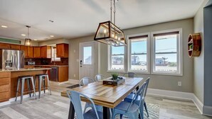 A modern kitchen with wooden cabinets, stainless steel appliances, and a dining area with a wooden table and blue chairs. - Huge Home- 1 min Walk to Beach- Perfect Location (Surf City)