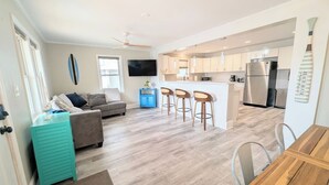 A modern kitchen with a central island, a dining area with a wooden table, and a living space with a sofa and a TV. - Huge Home- 1 min Walk to Beach- Perfect Location (Surf City)