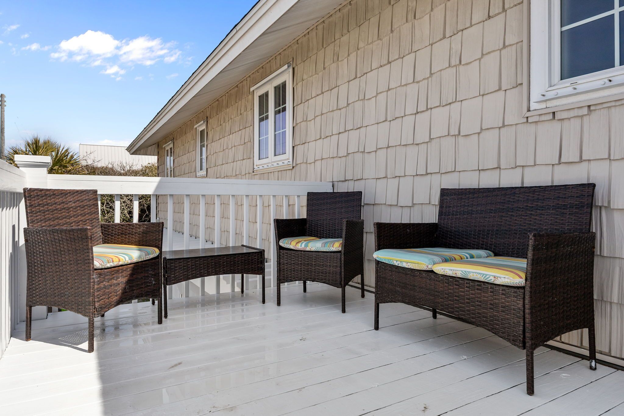 Une terrasse couverte, aménagée avec des meubles en osier et dotée d’une balustrade blanche.