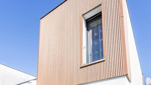 Um edifício moderno com fachada de madeira, grandes portas de correr de vidro e um deck de madeira.