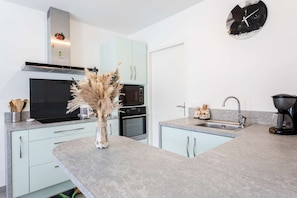 A modern kitchen with a built-in oven, microwave, and a decorative vase on the counter. - Maison climatisée avec jardin (BISCARROSSE)