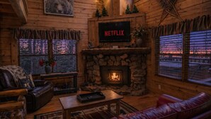 A cozy cabin interior with a stone fireplace, leather furniture, a mounted television, and a bear-themed decor. - Rustic Pet Friendly Cabin in Pigeon Forge! (Pigeon Forge)