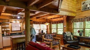 A cozy cabin interior with a kitchen, dining area, and living room furnished with a red sofa, patterned chairs, and a leather armchair. - Rustic Pet Friendly Cabin in Pigeon Forge! (Pigeon Forge)