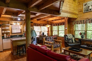 A cozy cabin interior with a kitchen, dining area, and living room furnished with a red sofa, patterned chairs, and a leather armchair. - Rustic Pet Friendly Cabin in Pigeon Forge! (Pigeon Forge)