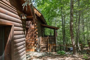 A log cabin with a porch, surrounded by a forest. - Rustic Pet Friendly Cabin in Pigeon Forge! (Pigeon Forge)