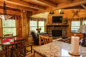 A log cabin interior with a stone fireplace, a television mounted above it, and a dining area with wooden furniture. - Rustic Pet Friendly Cabin in Pigeon Forge! (Pigeon Forge)