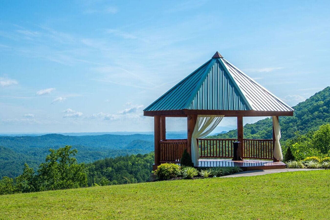Un belvédère doté d’un toit en métal, d’une terrasse en bois et offrant une vue sur un paysage montagneux.