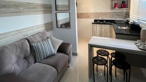 Una sala de estar moderna con sofá, una mesa de comedor con sillas, una zona de cocina con electrodomésticos y una lámpara de techo.