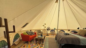 Une tente avec un lit, une chaise rouge, une petite table, un ventilateur et une lampe.