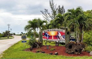 Un panneau d’accueil à l’entrée d’Everglades City, avec une route et des palmiers en arrière-plan.