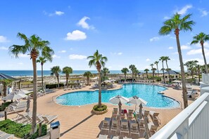 A pool area with lounge chairs and palm trees, overlooking a beach.