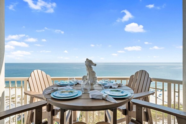 A table set for four with plates, glasses, and a decorative item on a balcony overlooking the sea.