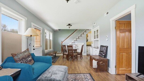 A spacious living room with a blue sofa, a stone bench, a dining area with wooden chairs, a staircase, and a TV stand. - River Road Cottage · 2BR Near Trails & Downtown (Missoula)