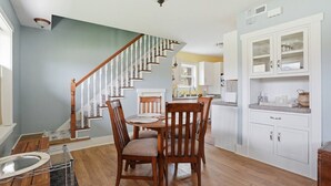 A dining area with a wooden table and chairs, a staircase, and a kitchen with white cabinets. - River Road Cottage · 2BR Near Trails & Downtown (Missoula)