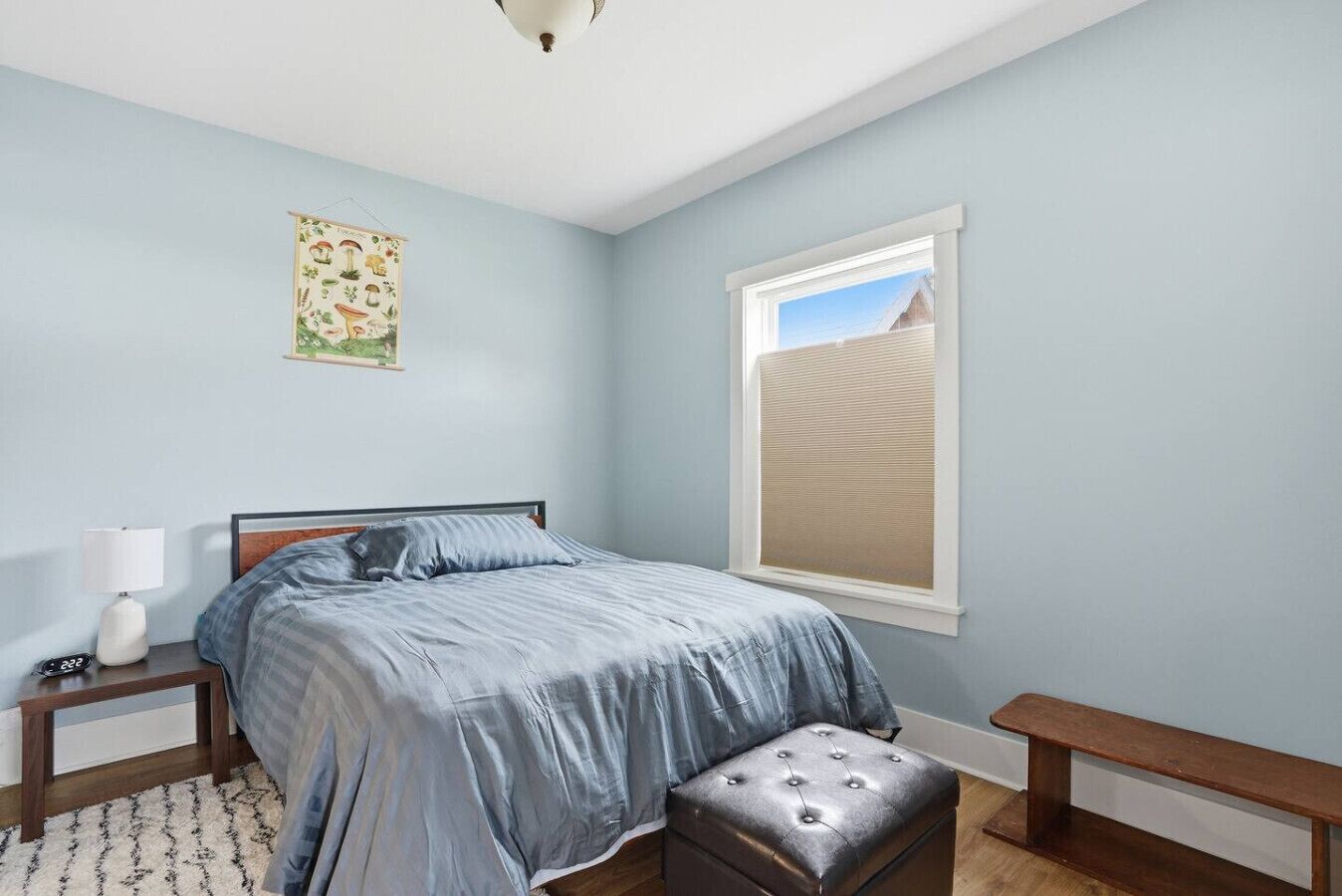 A bedroom with a bed, bedside table, lamp, and a window with a view of sand dunes.