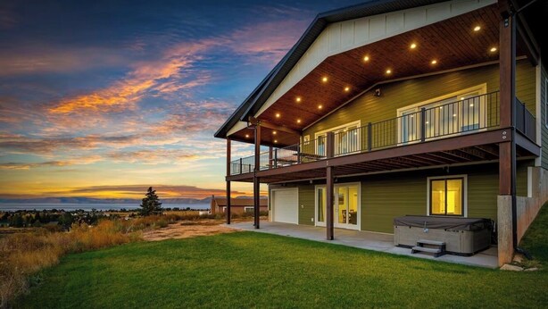 A modern two-story house with a covered patio, a garage, and a view of the ocean at sunset.