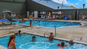 A swimming pool area with multiple pools, a lifeguard stand, and a covered structure in the background.