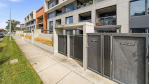 A modern multi-story building with a flat roof, large windows, and a gated entrance.