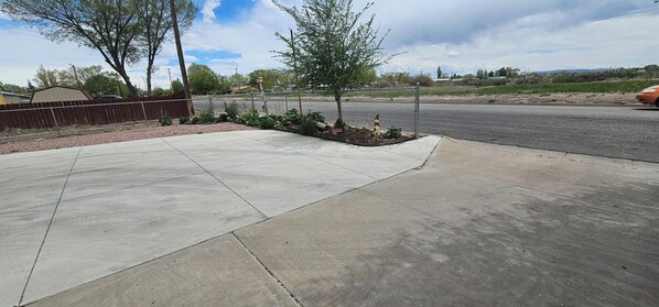 A paved area with a fence, a small tree, and a road in the background. - Spacious 3 bedroom and 1.5 bathroom fully fenced around for pets and childrens (Alamosa)