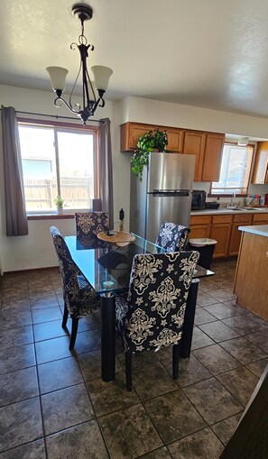 A dining area with a glass table, patterned chairs, a chandelier, a refrigerator, and wooden cabinets. - Spacious 3 bedroom and 1.5 bathroom fully fenced around for pets and childrens (Alamosa)