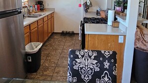 A kitchen with wooden cabinets, a stainless steel refrigerator, and a dining area with a woven chair.