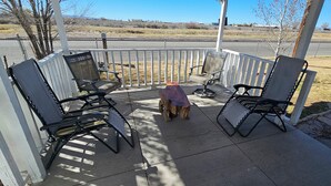 A covered patio with outdoor seating, a small table, and a view of a parking lot and distant landscape.
