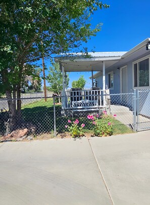 A residential house with a covered porch, a fenced yard, and a clear blue sky.