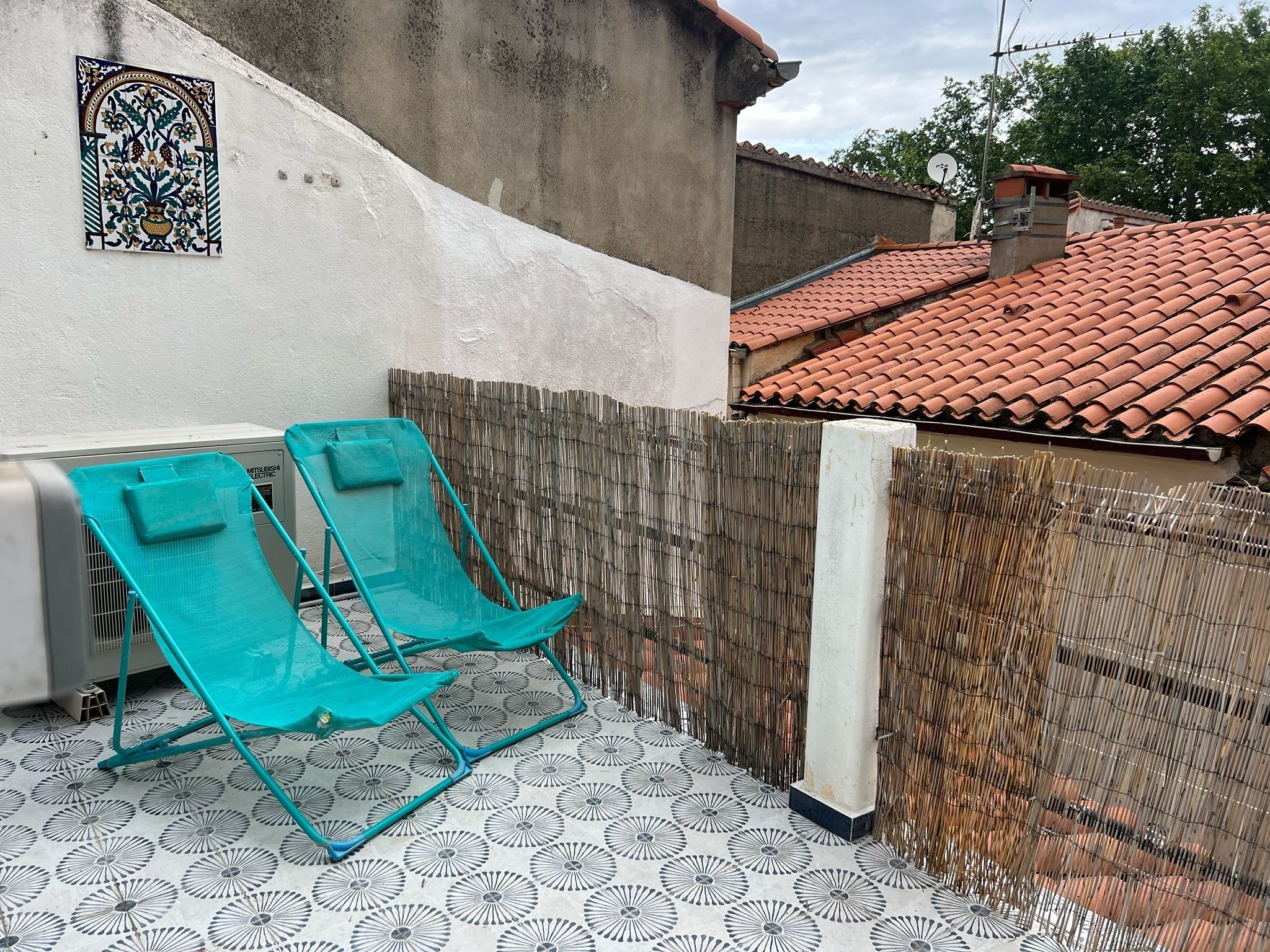A patio with two turquoise lounge chairs, a decorative wall tile, and a red-tiled roof.