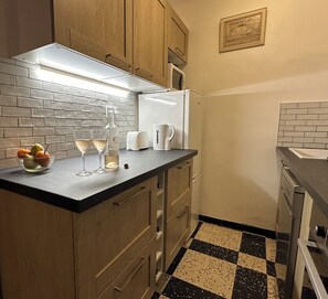 Eine kleine Küche mit Holdekor, einem schwarz-weißen Schachbrettfußboden, einem Kühlschrank, einem Toaster und einer Champagnerflasche.