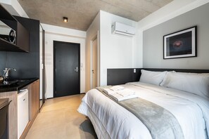Ein modernes Hotelzimmer mit einem Bett, einer kleinen Küchenzeile, einer Tür und einer Klimaanlage.